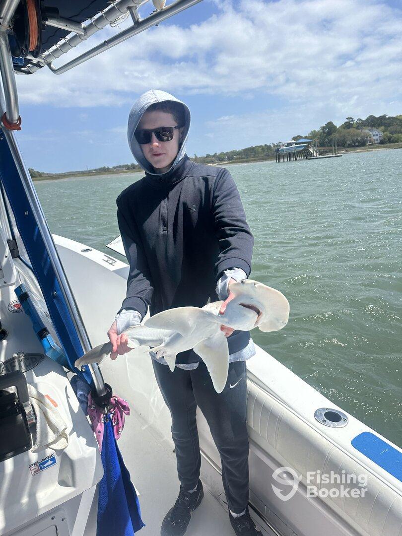 A young angler proudly displaying a caught shark while aboard a fishing boat, showcasing a successful day on the water.