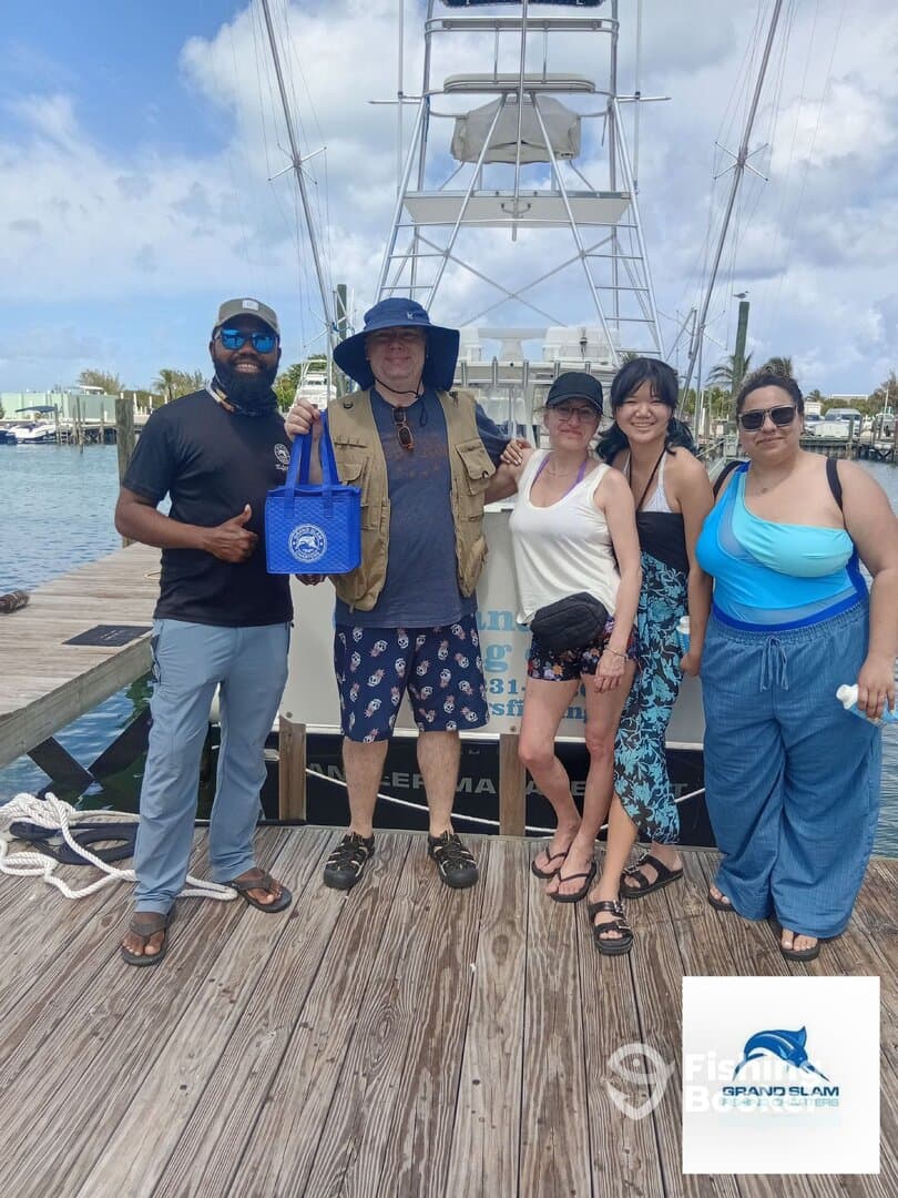 A group of five individuals posing together on the dock in front of a fishing boat, showcasing a fun day out on the water.