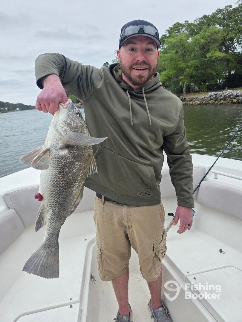 Angler proudly displaying a large striped bass while fishing from a boat.