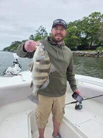 Angler proudly displaying a large striped bass while fishing from a boat in a scenic waterway.