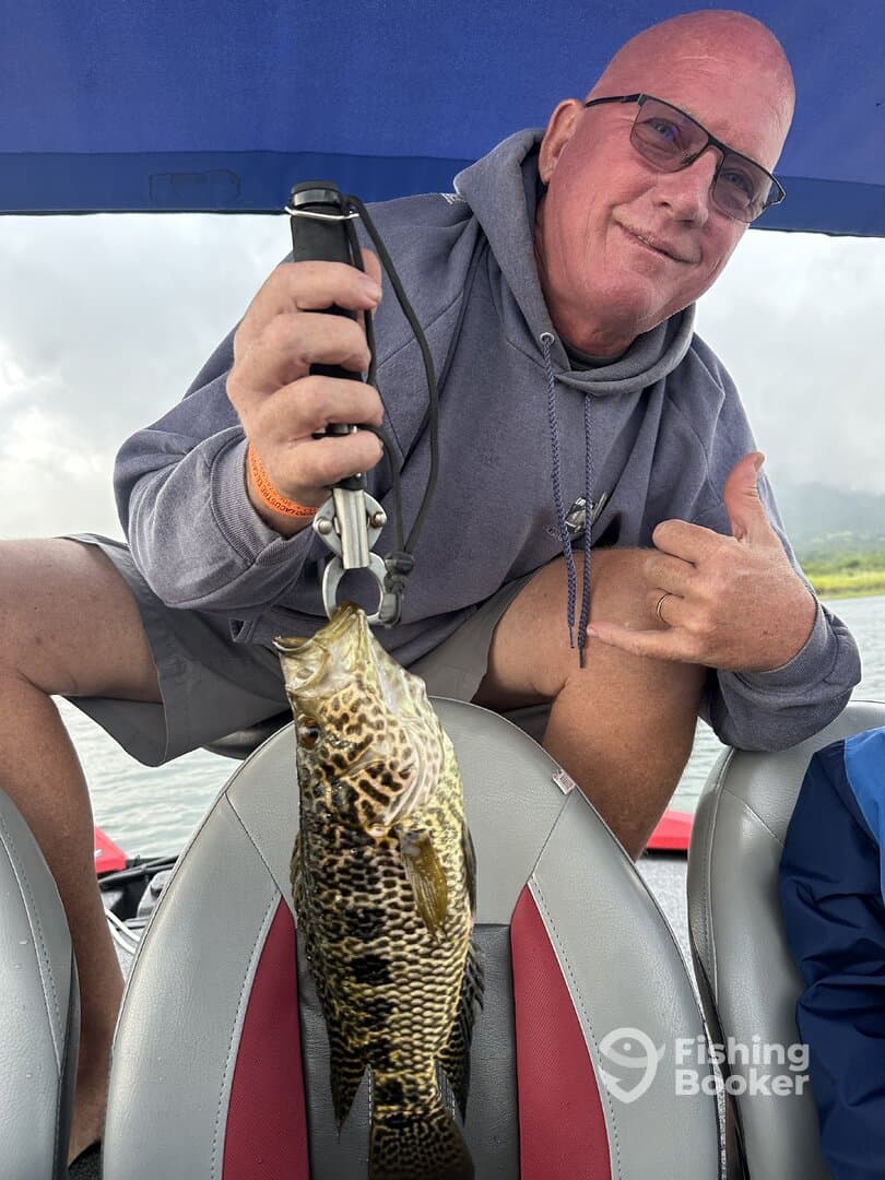 Angler proudly displaying a large Largemouth Bass while seated in a fishing boat, showcasing a successful day on the water.