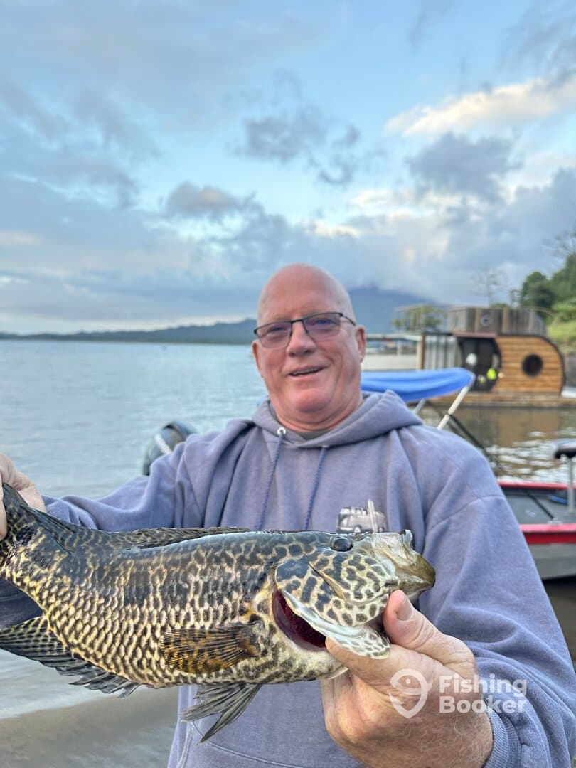 Angler proudly displaying a large Leopard Grouper caught during a fishing trip on a scenic lake.