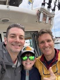 A group selfie taken on a fishing boat, featuring two adults and a child, showcasing a fun day on the water.