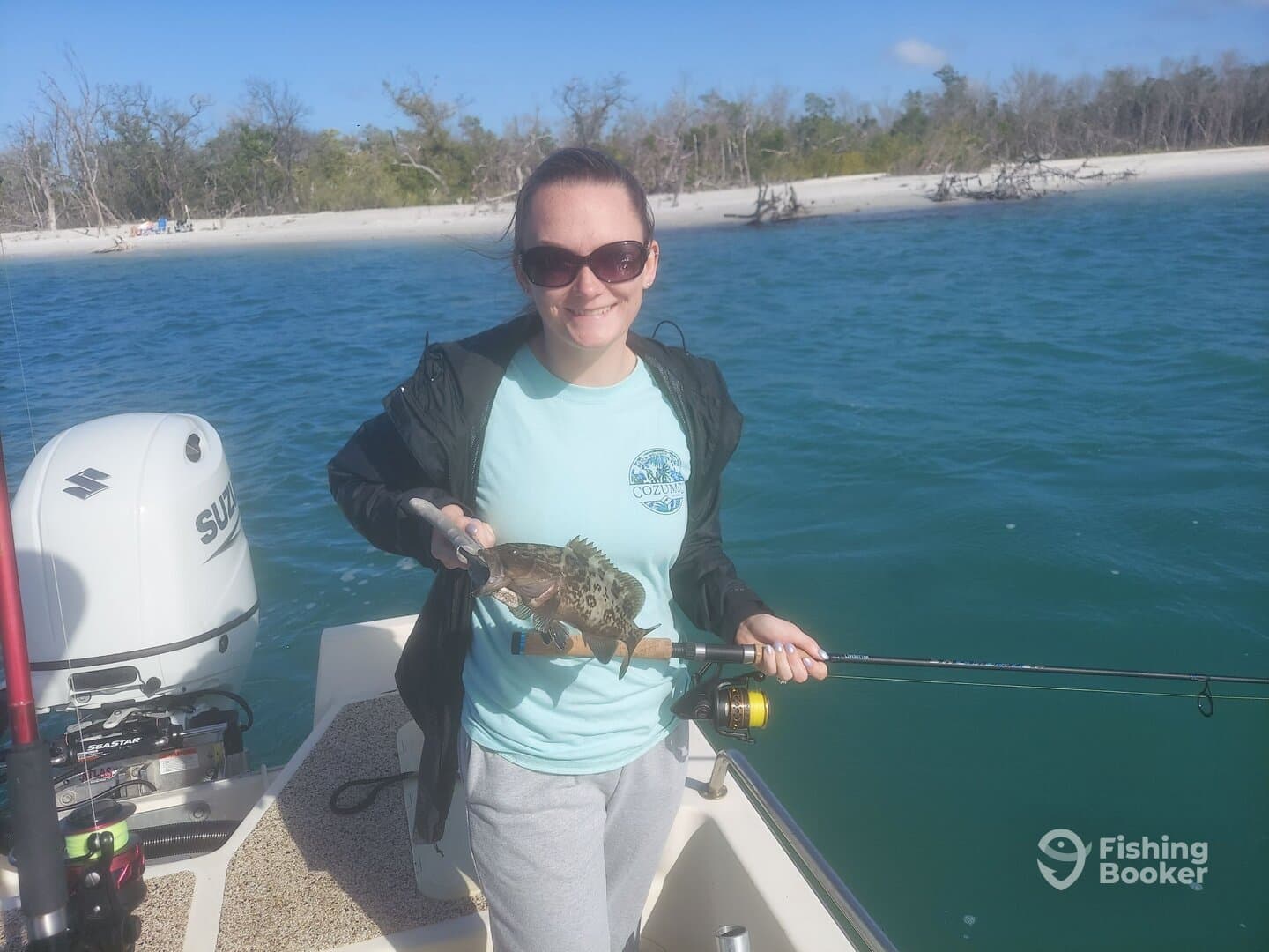 Angler holding a colorful Grouper while fishing from a boat in a scenic coastal environment.