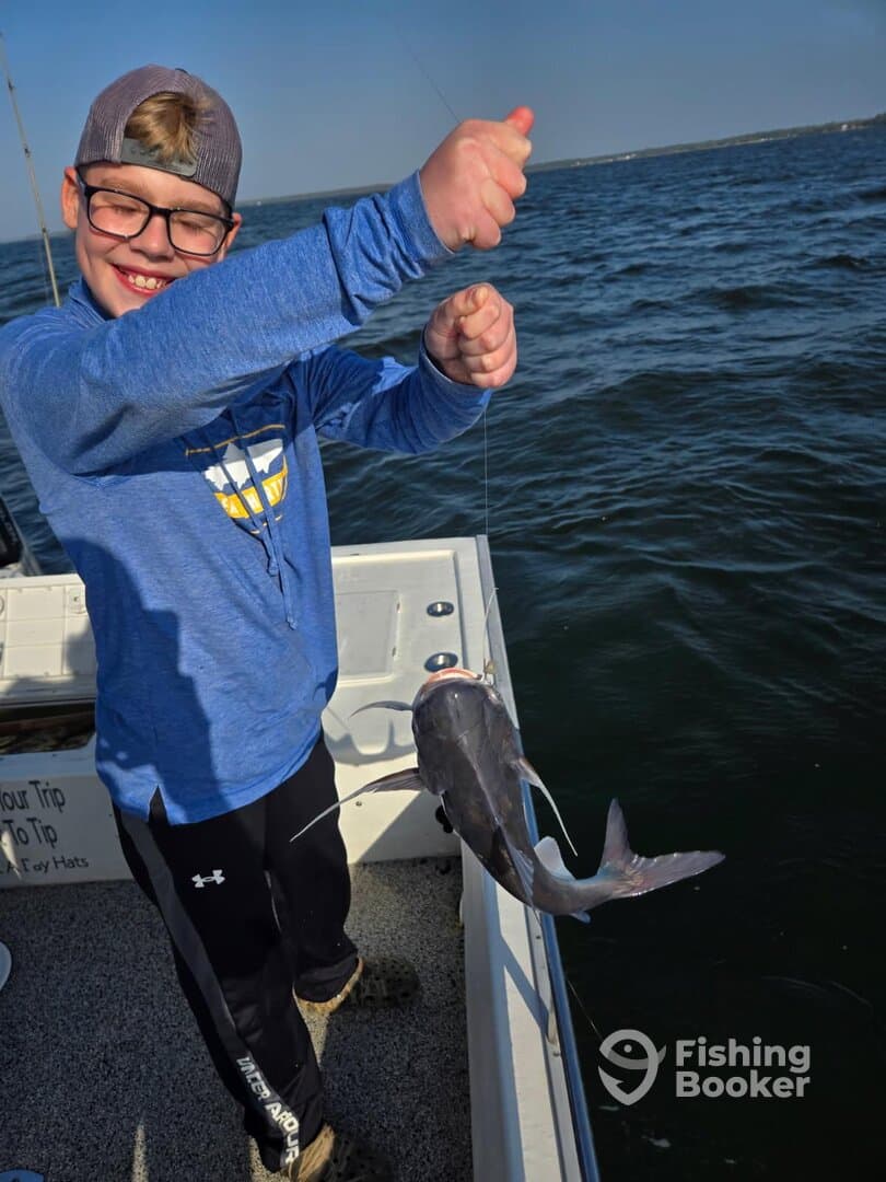 A young angler proudly displaying a caught catfish while fishing on a boat.