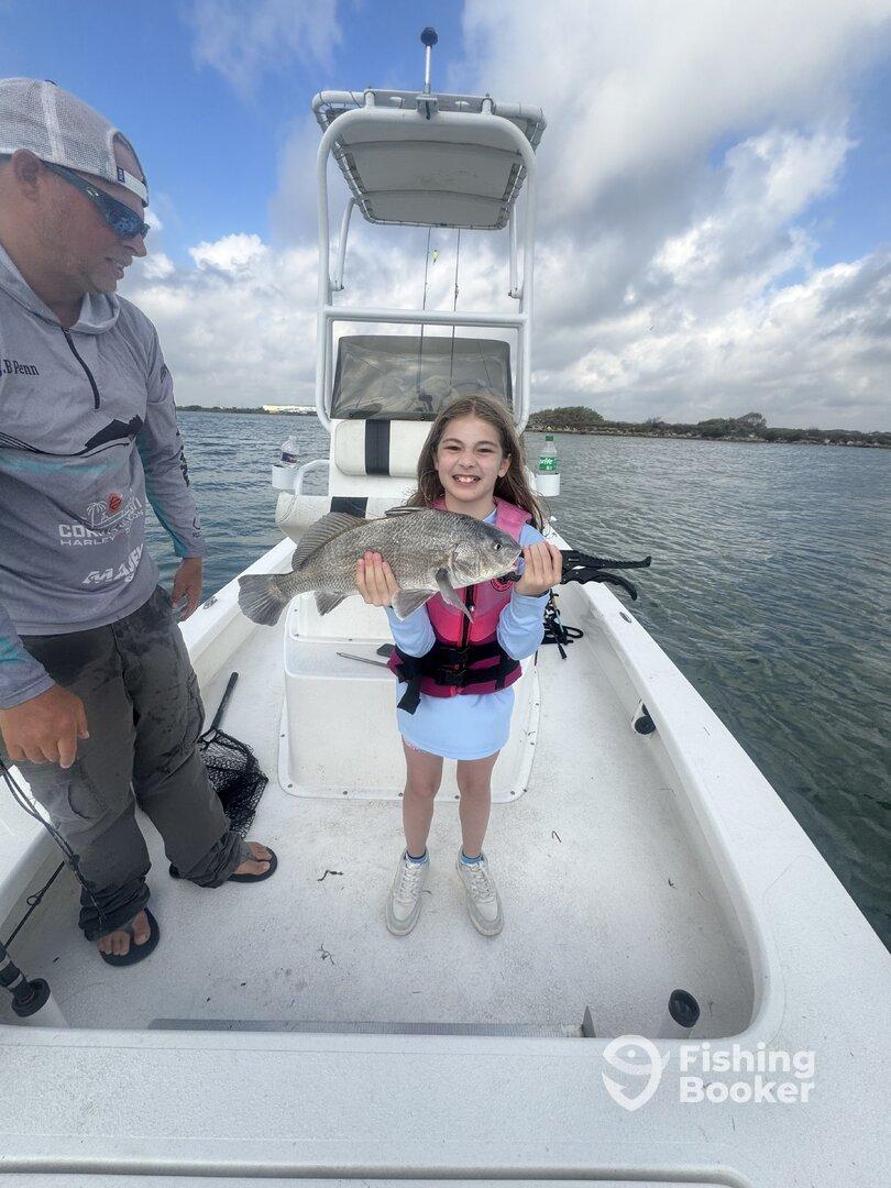 A young angler proudly displaying a large Black Drum while fishing on a boat, showcasing a fun family fishing experience.