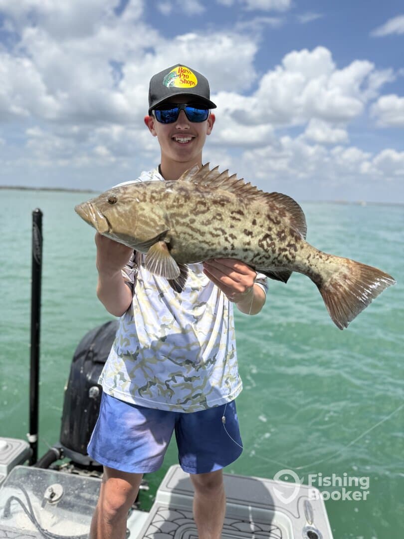 A young angler proudly displaying a large Grouper while fishing on a sunny day.