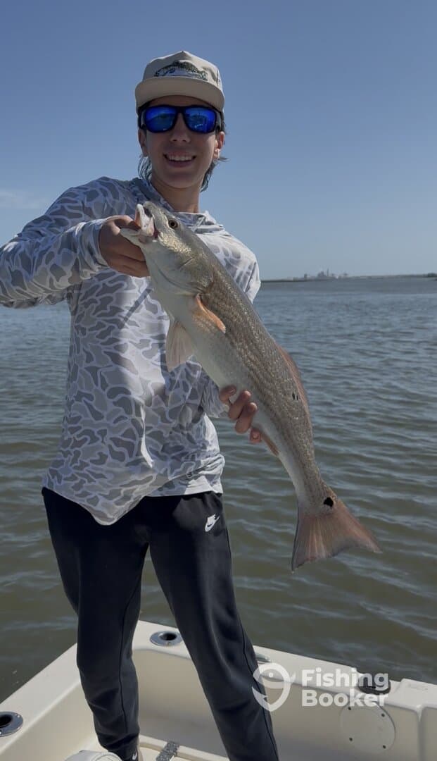 Young angler proudly holding a large Redfish while fishing on a boat.