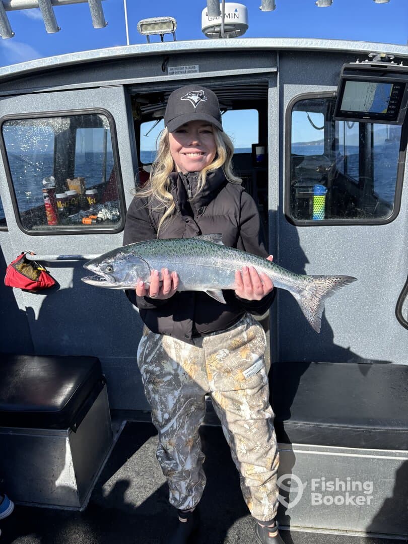 A proud angler holding a large Rainbow Trout aboard a fishing charter, showcasing a successful day on the water.