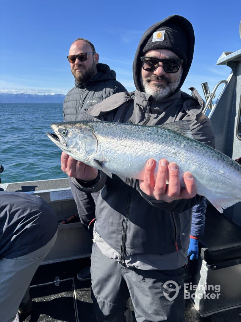 Angler proudly displaying a large Salmon while fishing on a boat, with a scenic ocean backdrop.