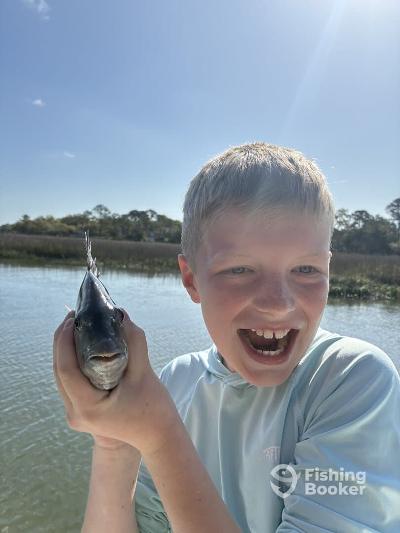A young angler excitedly holds up a fish while fishing in a scenic waterway, showcasing the joy of fishing.