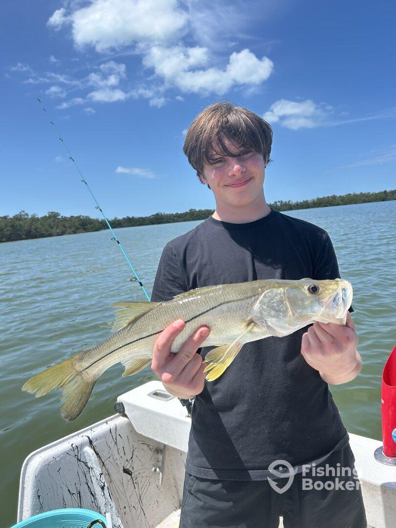 A young angler proudly displaying a Snook caught while fishing in a scenic coastal environment.