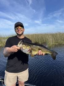 Angler proudly displaying a large Largemouth Bass while fishing in a scenic freshwater environment.