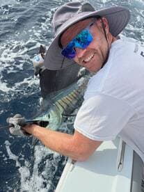Angler actively reeling in a large Sailfish while enjoying a deep-sea fishing adventure.