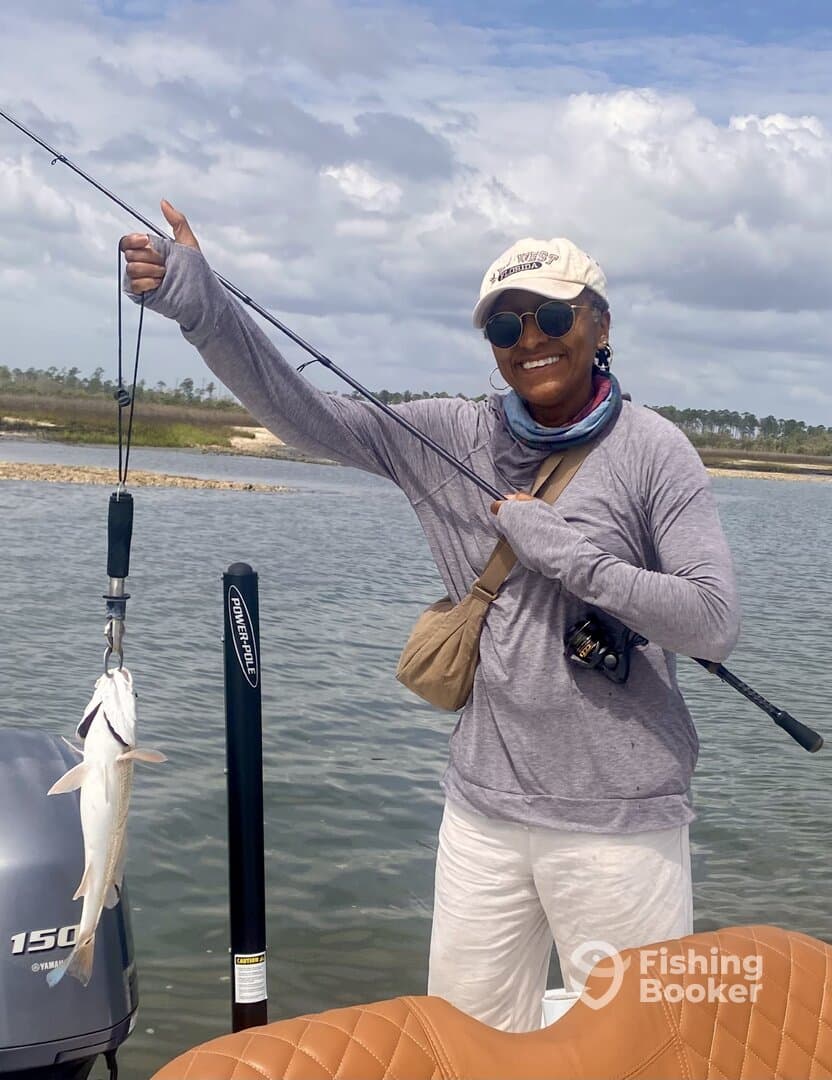 An angler proudly displaying a caught fish while fishing from a boat in a scenic waterway.