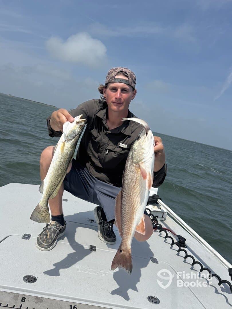 A young angler proudly displaying a Speckled Trout and a Redfish while fishing on a boat in coastal waters.