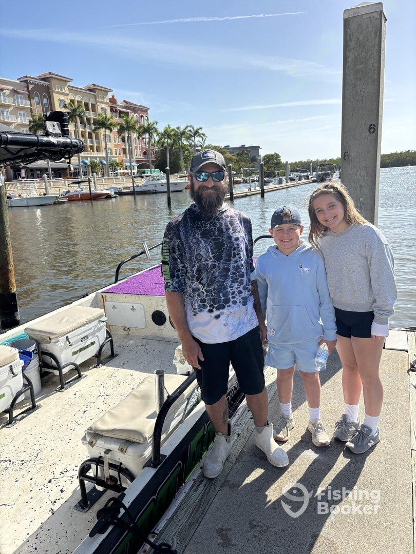 A family poses on the dock next to their boat, with a scenic waterfront view in the background.