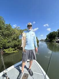 Angler proudly displaying a Redfish while fishing in a scenic waterway, surrounded by mangroves.