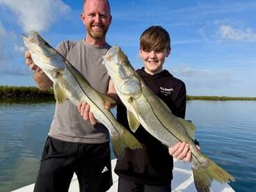 A proud father and son duo displaying their impressive Snook catch while enjoying a day on the water.