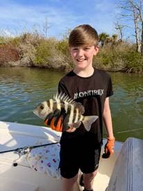 A young angler proudly displaying a Sheepshead fish while fishing from a boat in a scenic waterway.