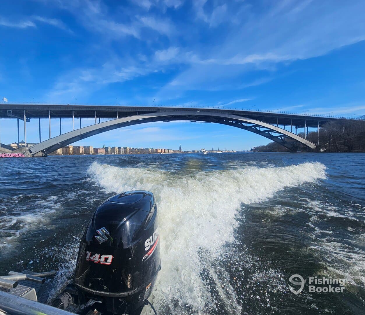 A scenic view of a boat's motor cutting through the water beneath a large bridge, showcasing the urban fishing environment.