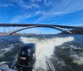 A scenic view of a boat's motor cutting through the water beneath a large bridge, showcasing the urban fishing environment.