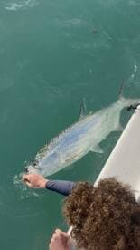 A young angler is reeling in a large Tarpon while fishing from a boat in clear waters.