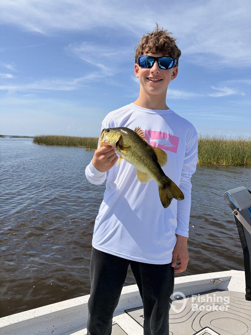 A young angler proudly displaying a large Largemouth Bass while fishing on a sunny day.
