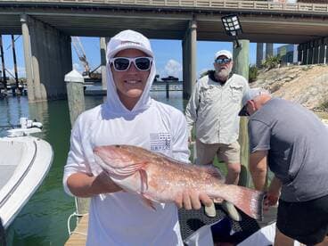 A young angler proudly displaying a large Red Snapper at the dock, with fellow anglers preparing for the next catch.