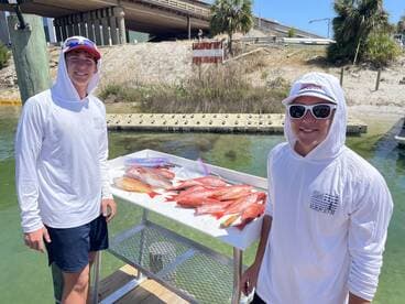 Two anglers proudly posing with a variety of Snapper on a catch board at a dock in Destin, showcasing their successful fishing trip.