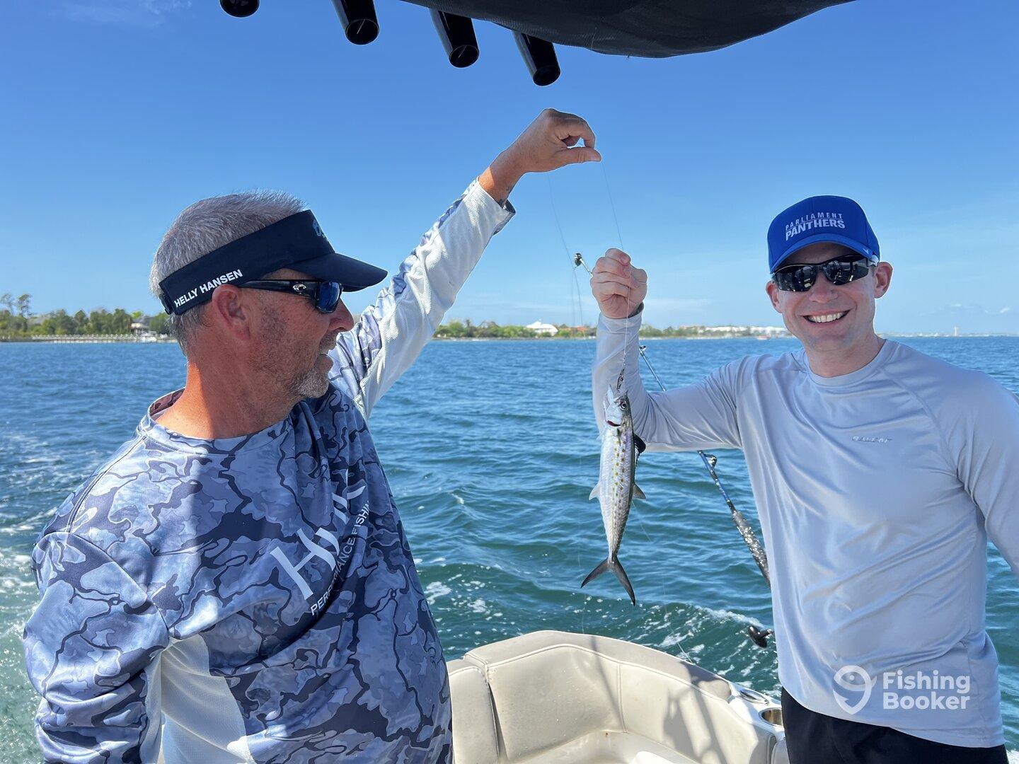 Two anglers on a boat celebrating a catch of a Spanish Mackerel during a sunny day on the water.
