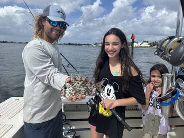 A young girl proudly holds a colorful fish while fishing with family on a boat, showcasing a fun day on the water.