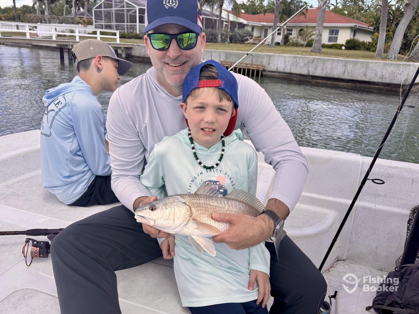 A young angler proudly displays a caught fish while fishing with family on a boat, showcasing a fun day on the water.