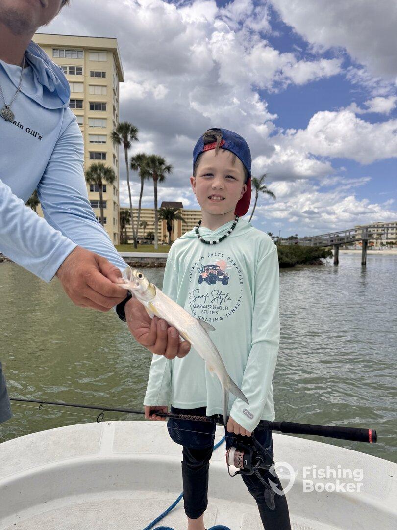 A young angler proudly displaying a small fish while fishing from a boat in a scenic coastal setting.