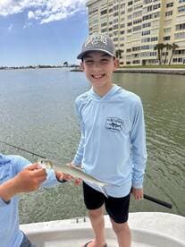 A young angler proudly displaying a small fish while fishing from a boat in Clearwater Beach.