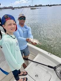 A young angler and a guide proudly displaying a caught fish while fishing from a boat in a coastal area.