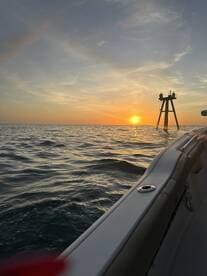 A scenic view of the sunset over the ocean, captured from the side of a boat, with a fishing structure visible in the distance.