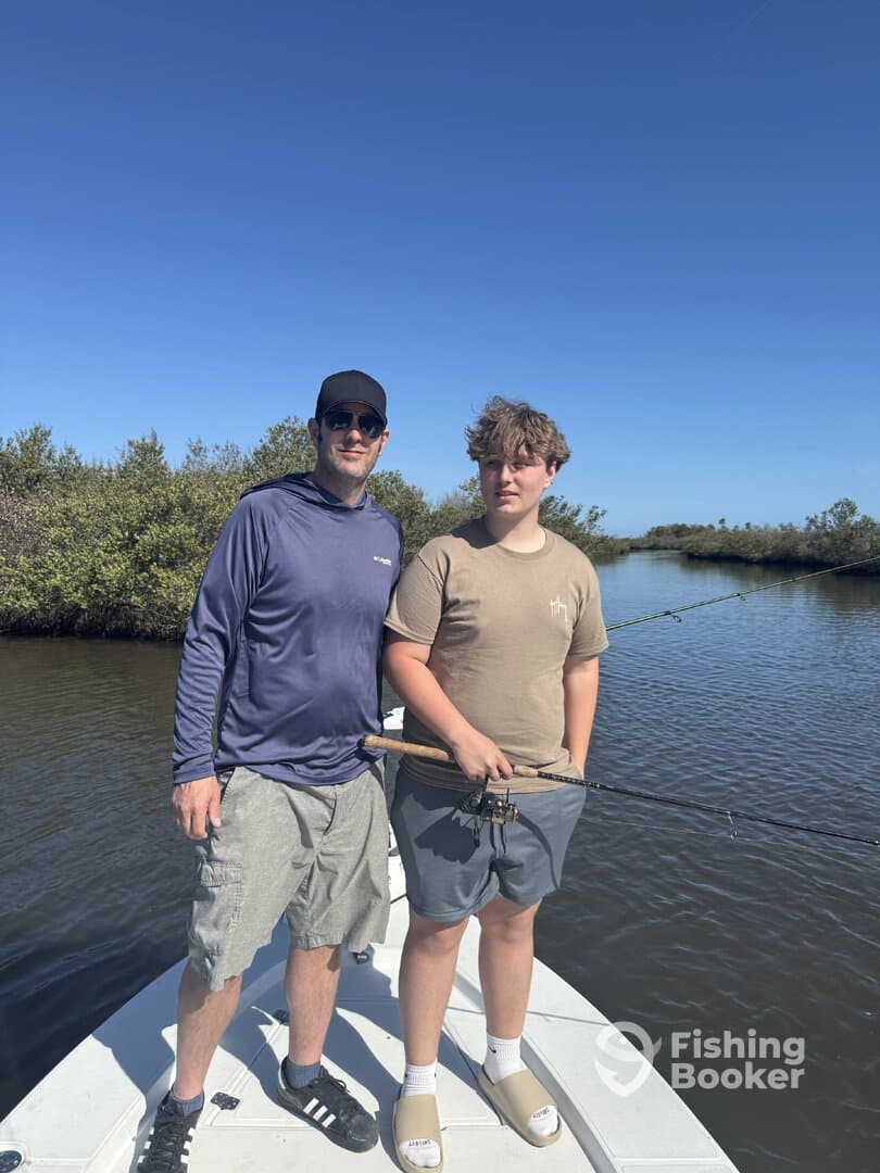 A father and son enjoying a fishing trip on a boat, surrounded by mangroves under a clear blue sky.