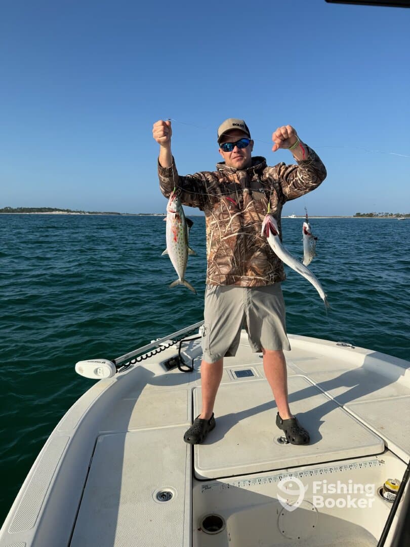 Angler proudly displaying three speckled trout while fishing from a boat in clear waters.