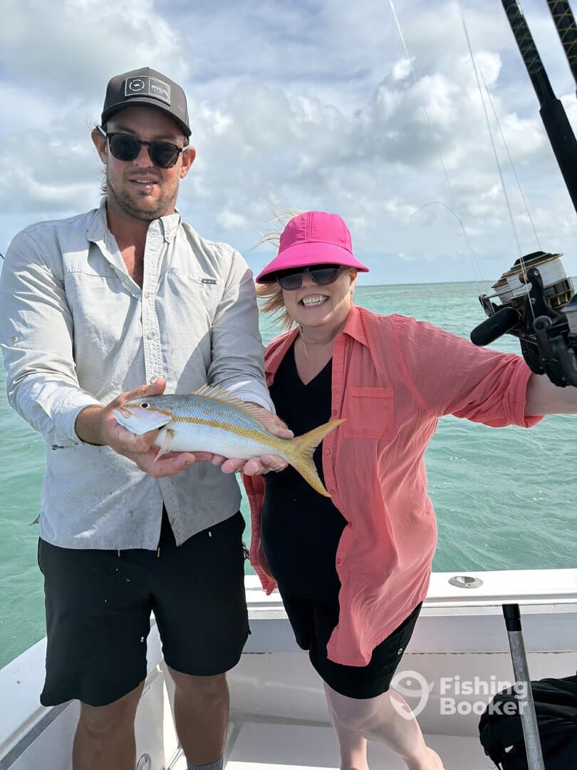 Two anglers proudly displaying a colorful Yellowtail Snapper while fishing on a sunny day.