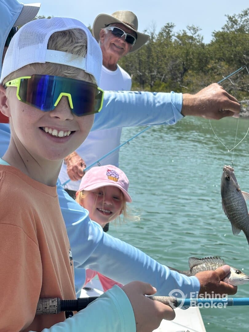 A young angler proudly displaying a fish while fishing with family on a sunny day, showcasing a fun and engaging fishing experience.