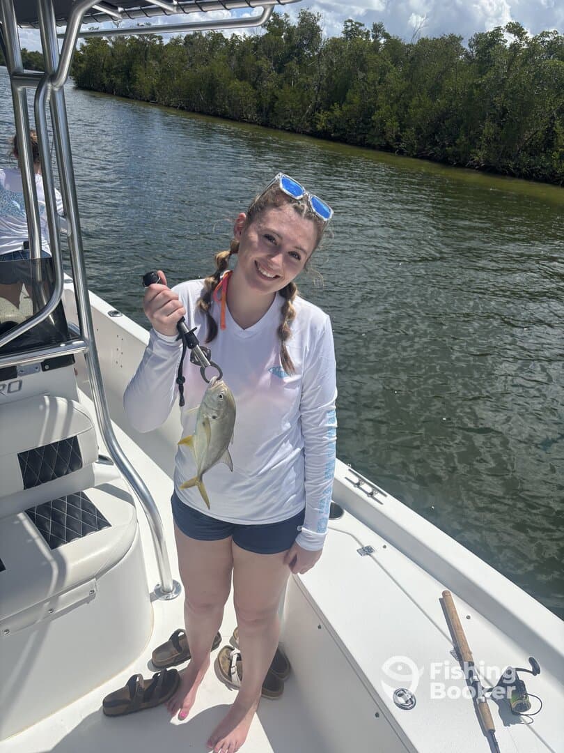 A young angler proudly displaying her catch, a small fish, while enjoying a day on the water in a boat surrounded by lush greenery.