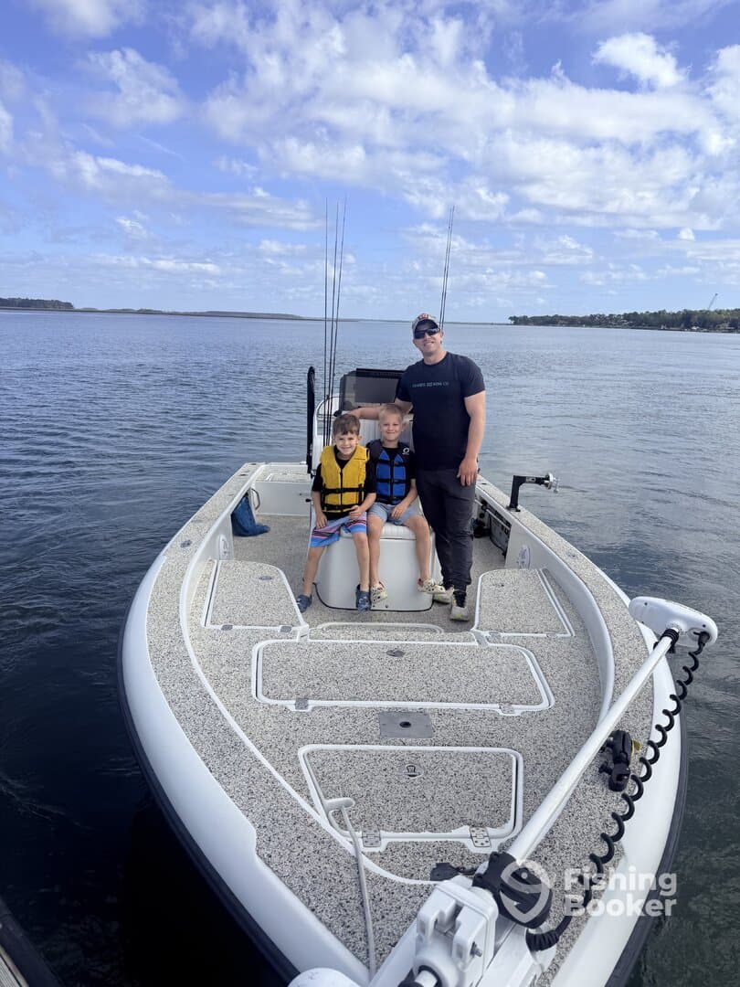 A family enjoying a day on a fishing boat, with two young boys wearing life jackets and a parent posing with them on the water.