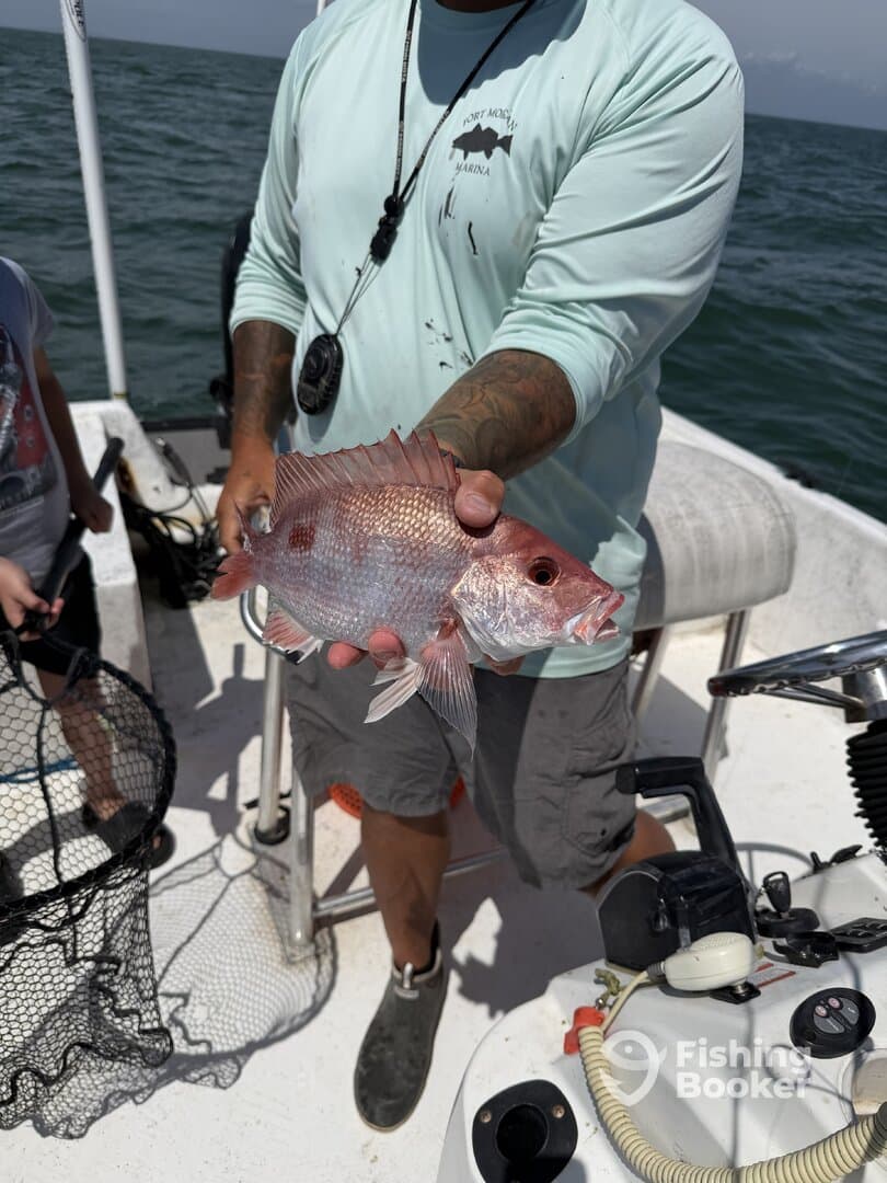 A proud angler displaying a freshly caught Snapper while fishing on a boat, with a child nearby.