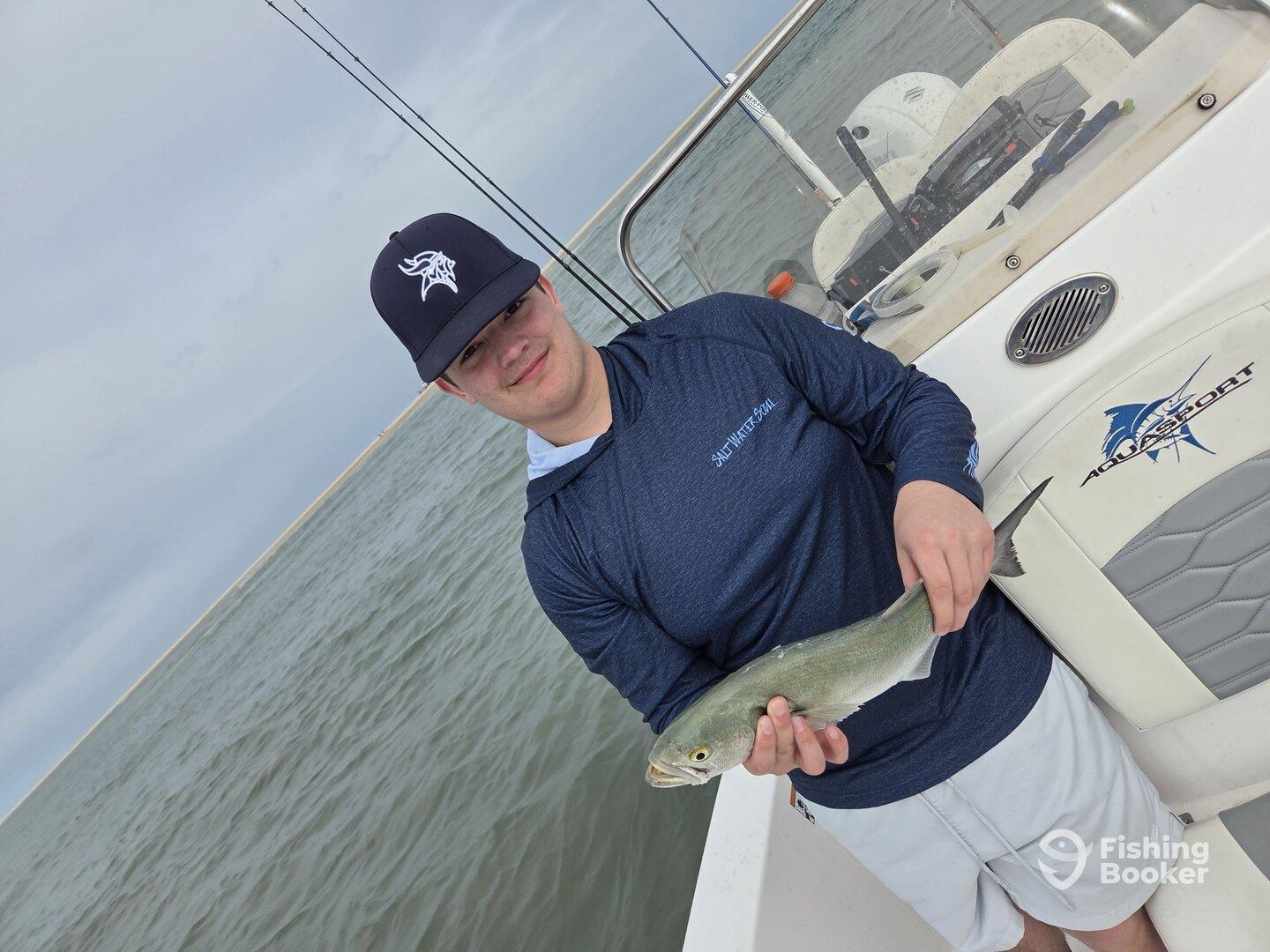 Young angler proudly holding a small fish on an Aquasport boat during a fishing trip.