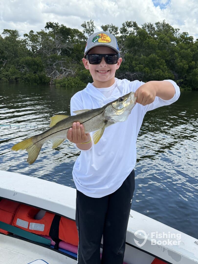 A young angler proudly displaying a Snook caught while fishing from a boat in a scenic coastal environment.