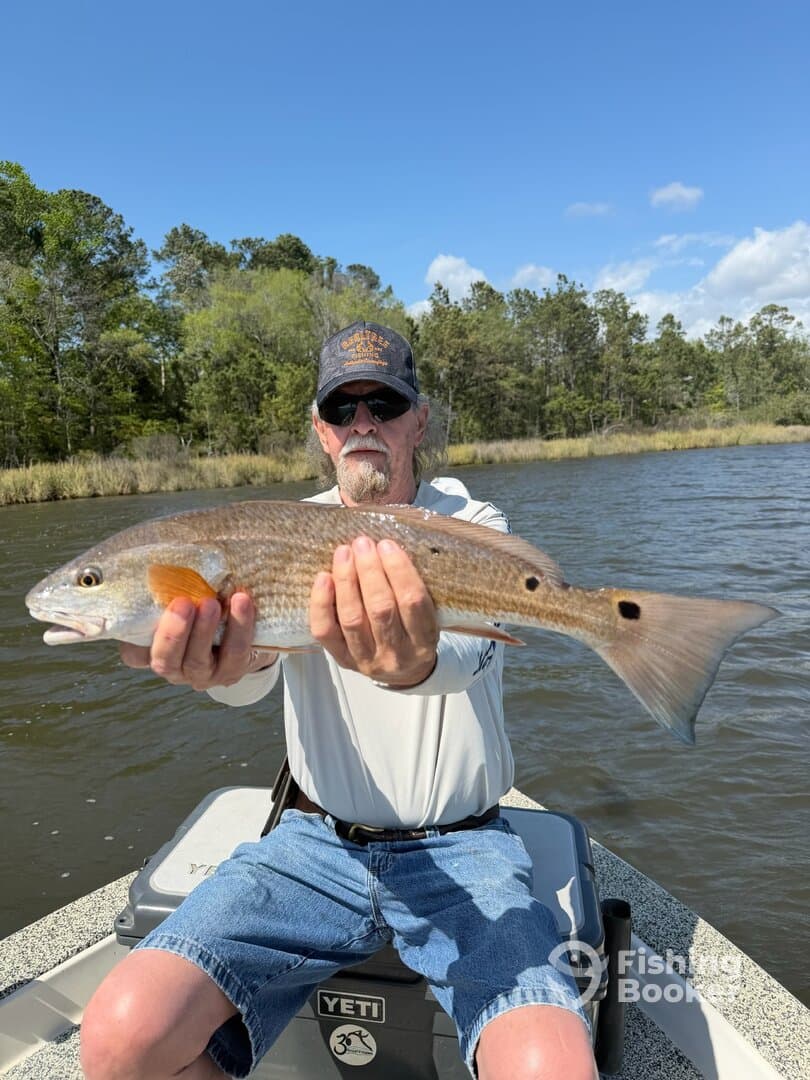 An angler proudly displaying a large Redfish while fishing on a calm waterway, showcasing a successful day on the water.