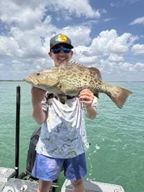 A young angler proudly displaying a large Grouper while fishing on a sunny day.