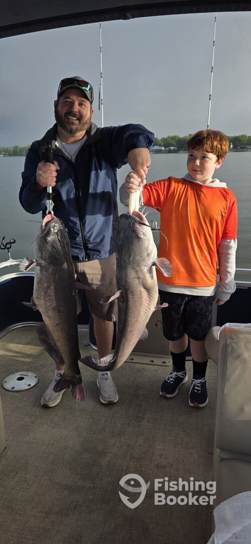 A proud angler and a young boy display their impressive catch of two large Catfish while fishing on a boat.