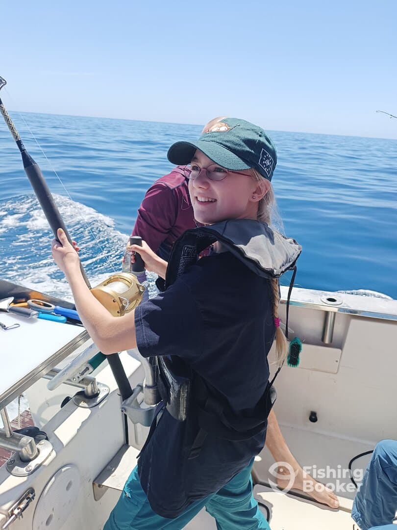 A young angler enthusiastically reeling in a catch while fishing on a boat in calm waters.